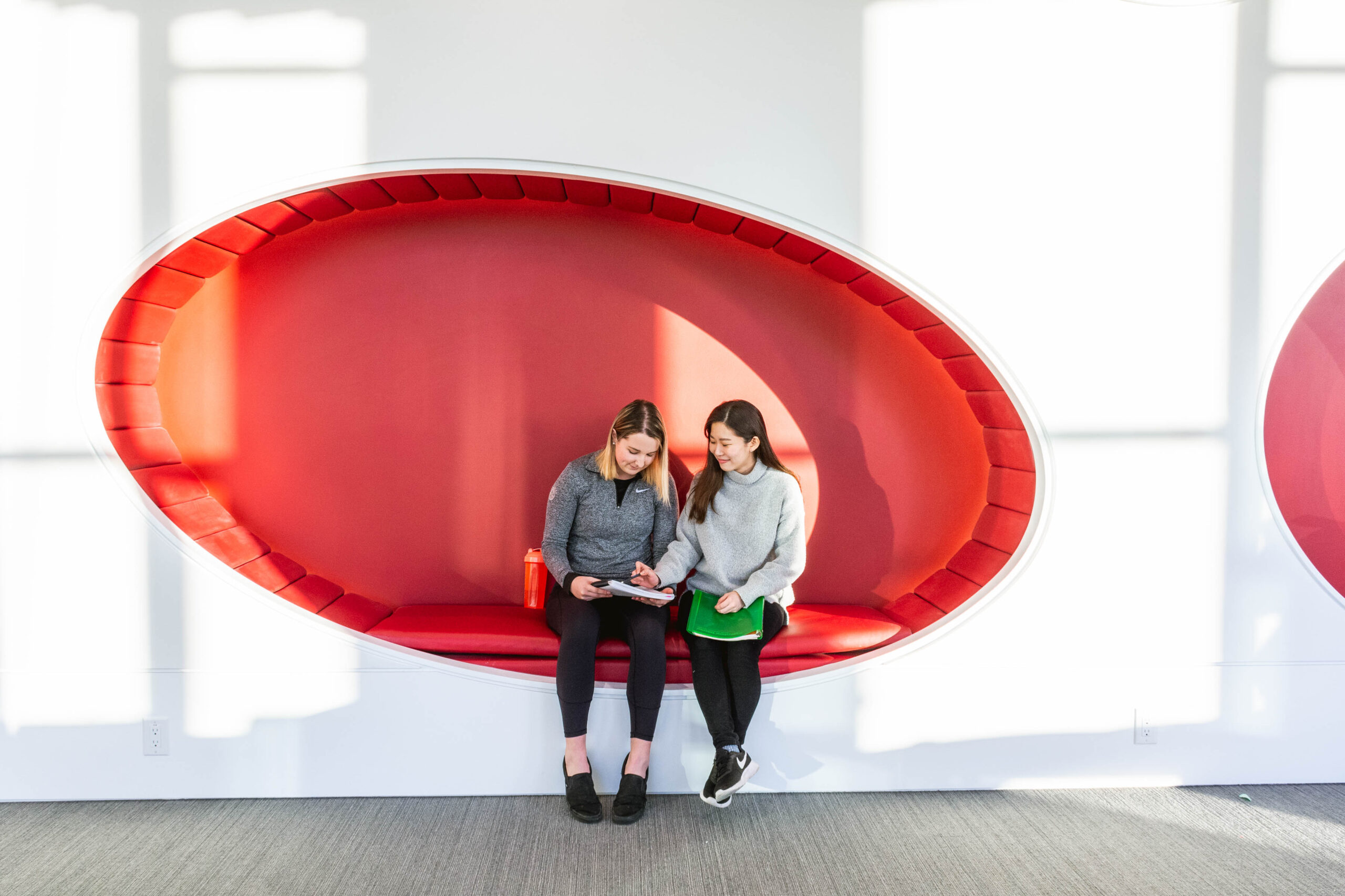 Two women discussing something in a notebook sitting in an interesting red booth