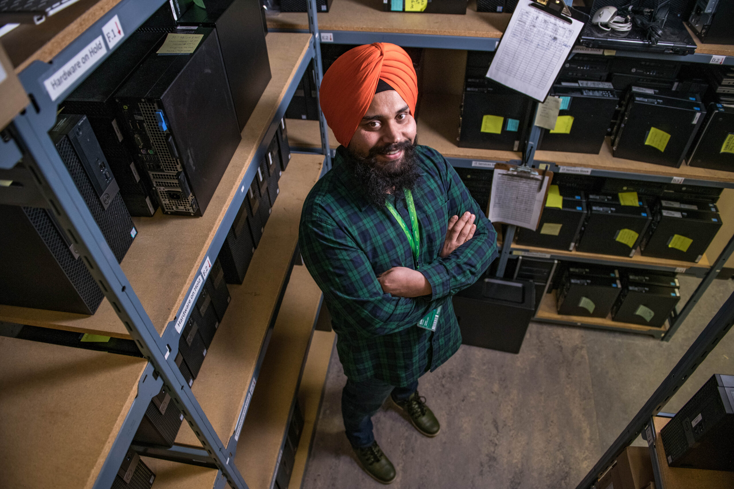 A young man with arms crossed, looking up at the camera surrounded by technology equipment