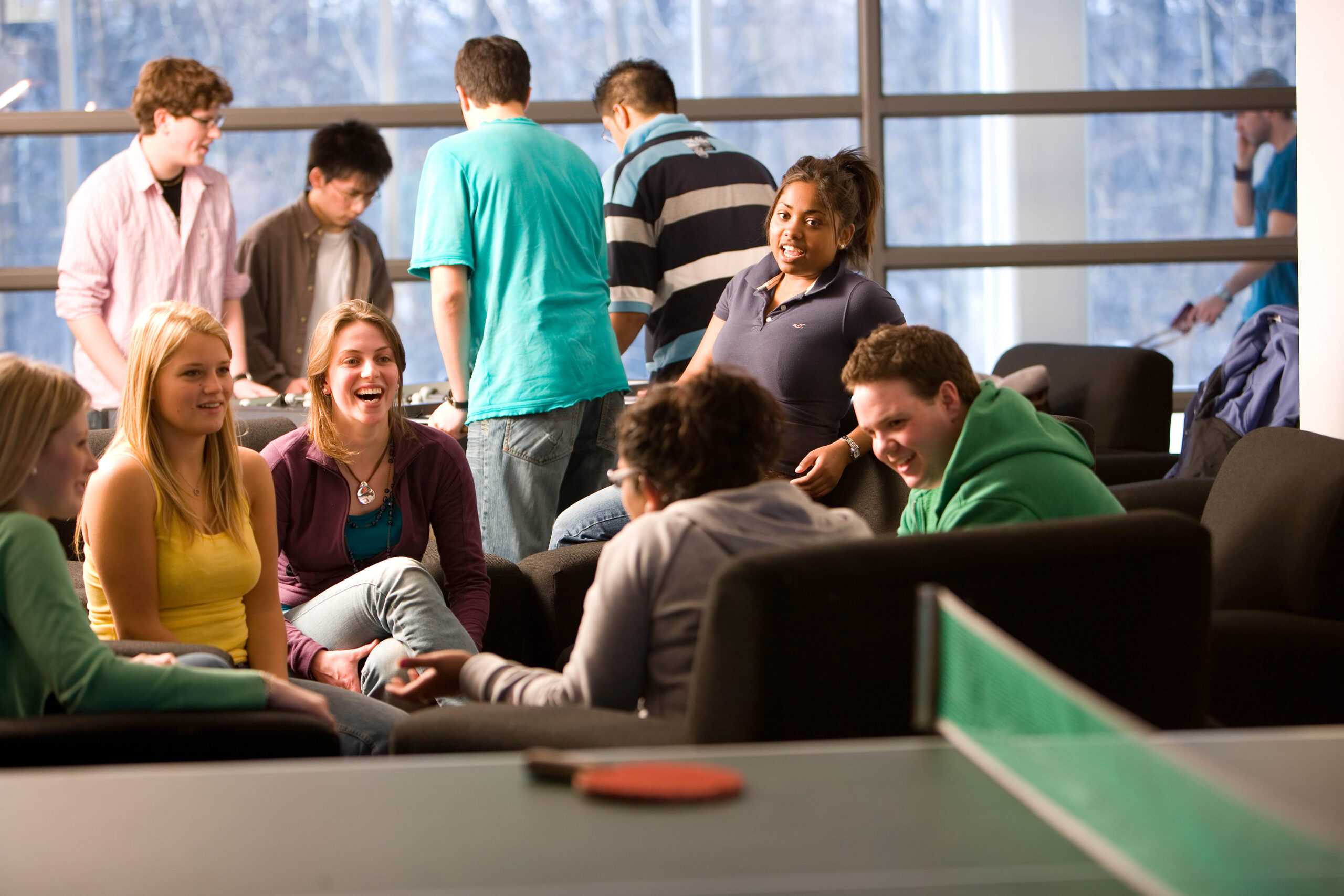 A large group of students having an animated conversation with a ping-pong table in the foreground