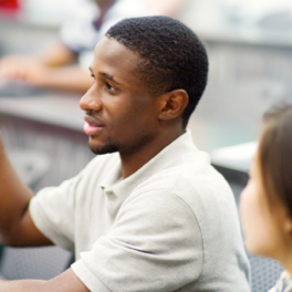 young man in a classroom with hand raised