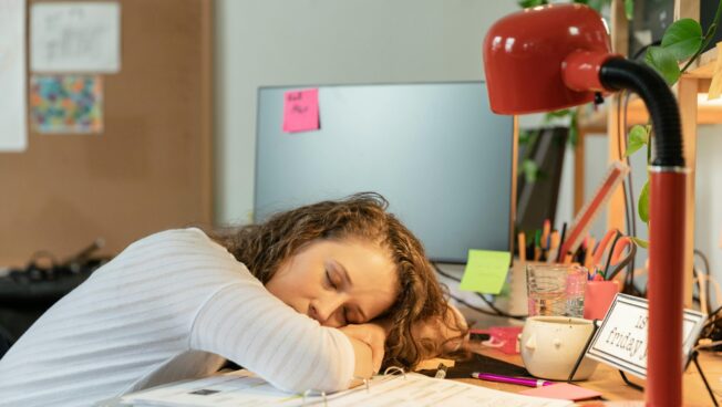 Student sitting at a desk surrounded by books and papers  with unfinished assignments.